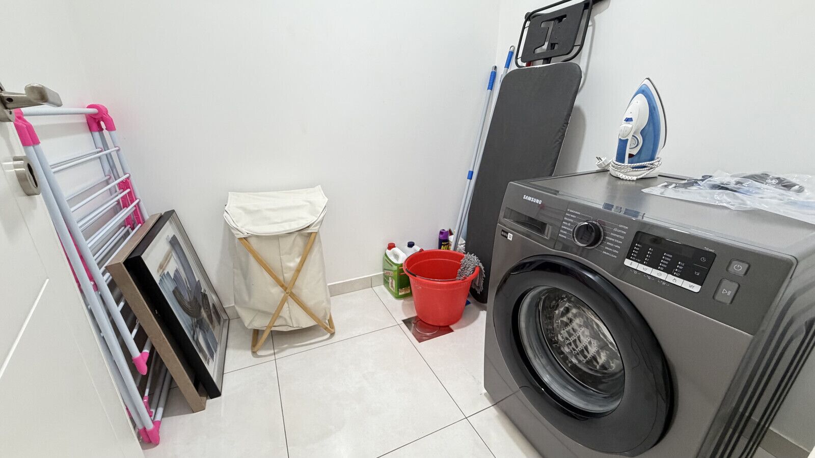 Een wasruimte met een wasmachine, een droogrek, een kleine prullenbak en een dweil.