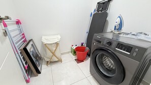 A laundry area with a washing machine, a drying rack, a small trash bin, and a mop.