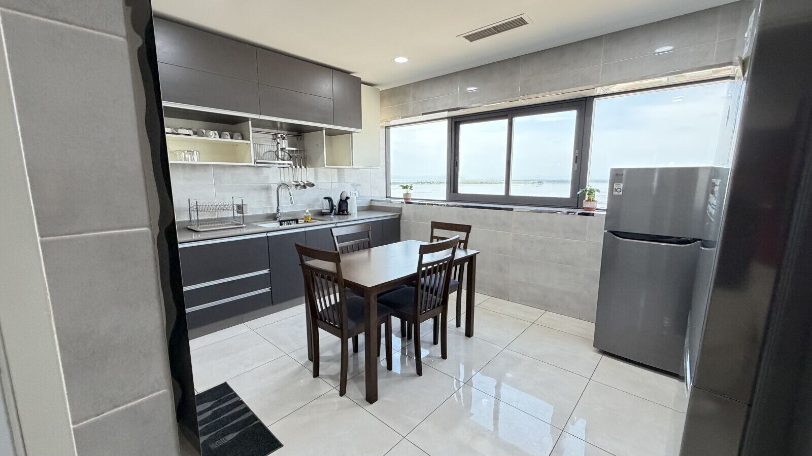 Una cocina moderna con una mesa de comedor y sillas, un refrigerador, y vistas al mar a través de amplios ventanales.