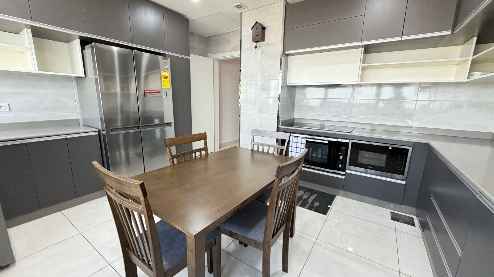 A modern kitchen with a dining table, chairs, stainless steel appliances, and grey cabinetry.