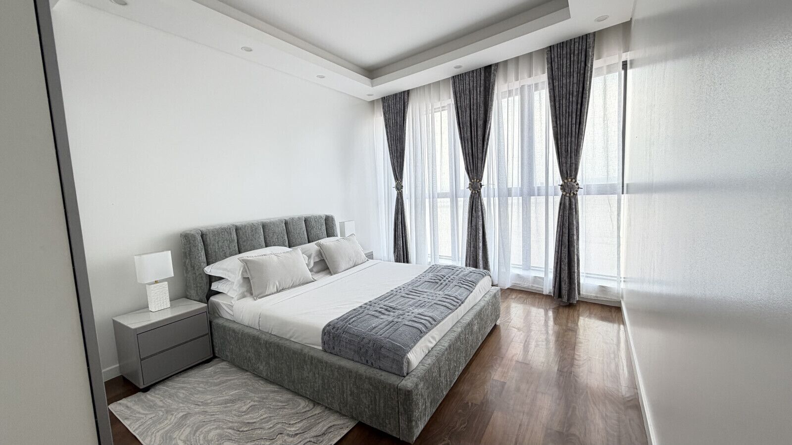 A modern bedroom with a large bed, bedside tables, and a view of the outdoors through sheer curtains.