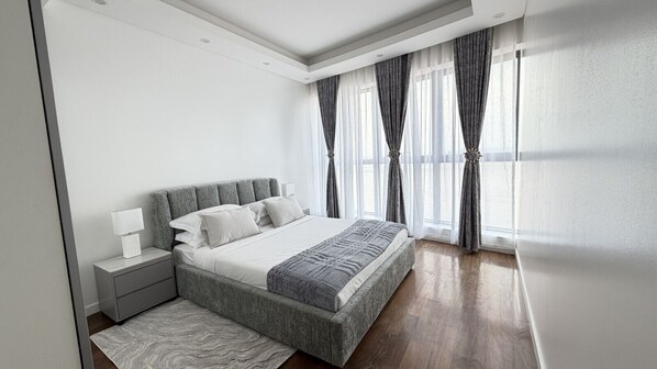 A modern bedroom with a large bed, bedside tables, and a view of the outdoors through sheer curtains.