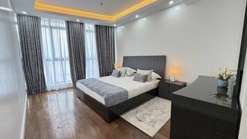 A modern bedroom with a large bed, bedside tables, and a desk with a lamp.