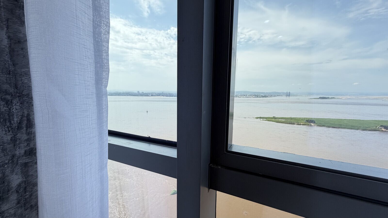 A window with a view of a river and distant buildings.