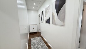 Een gang met een witte muur, een kamerbreed tapijt met dessin en abstracte wanddecoratie.