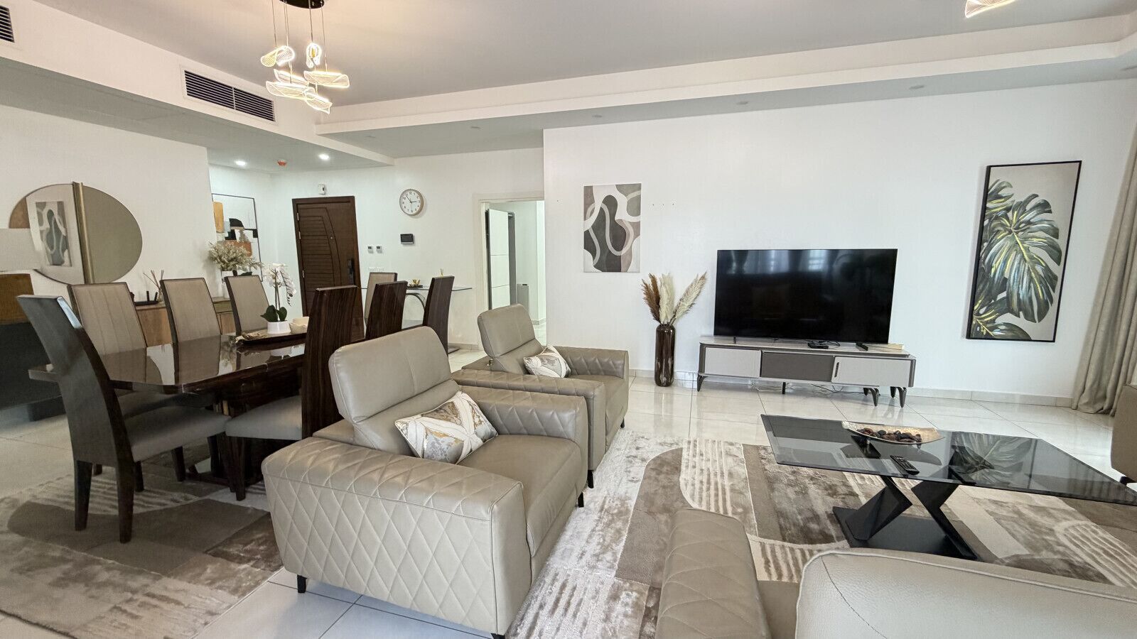 Una sala de estar moderna con un conjunto de sofás, un televisor de pantalla plana y un comedor con sillas y una mesa.