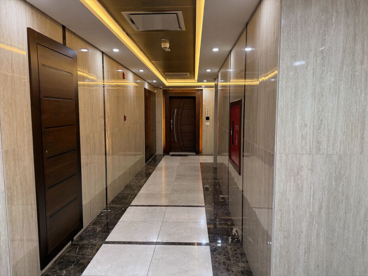 A corridor with a marble floor, wooden doors, and recessed lighting.