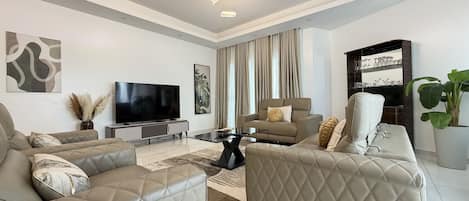 A modern living room with a flat-screen TV, leather sofas, a glass coffee table, and a large potted plant.