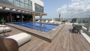 Area piscina sul tetto con poltrone relax, una piscina e vista sullo skyline della città.
