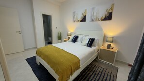 Ein Schlafzimmer mit einem Bett, Nachttischen, einer Wand mit Kunstwerken und einer Tür.
