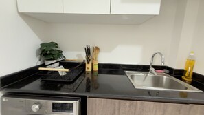 A kitchen with a black countertop, stainless steel sink, and a dish rack. - Elegant 8th Floor River View Apartment Eloge Tower (Kinshasa)