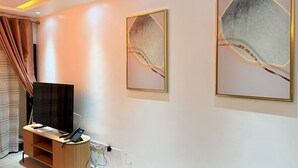 Habitació d'hotel amb televisió de pantalla plana sobre un suport de fusta, un telèfon i dues obres d'art abstractes enmarcades a la paret.