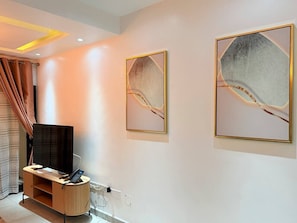 A hotel room with a flat-screen TV on a wooden stand, a telephone, and two framed abstract artworks on the wall. - Kintambo Velodrome apartment in a secure building with Gym (Kinshasa)