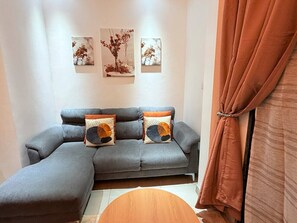 A grey sofa with two patterned cushions, a small round table, and a brown curtain. - Kintambo Velodrome apartment in a secure building with Gym (Kinshasa)