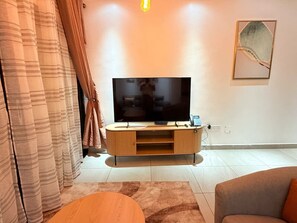 Ein Wohnzimmer mit Flachbildfernseher auf einem Holzständer, einer Couch, einem Couchtisch und einem Gemälde an der Wand.