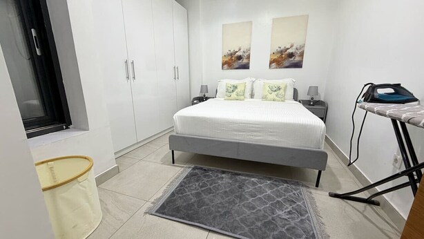 A bedroom with a bed, a nightstand, a window, and a wall-mounted ironing board.