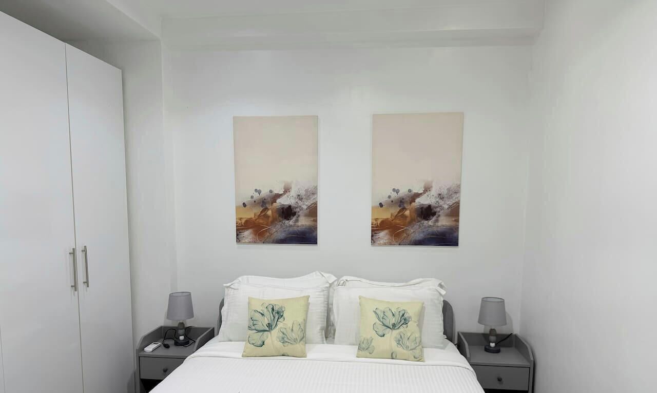 A hotel room with a bed, two nightstands, a wardrobe, and two abstract paintings on the wall.