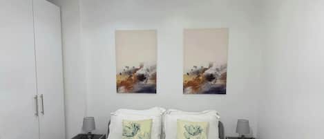 A hotel room with a bed, two nightstands, a wardrobe, and two abstract paintings on the wall.