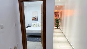 A hotel corridor with a bed in the background, a potted plant, and a door leading to another room. - 1 bedroom Apartment in Kintambo Velodrome secure clean  with gym (Kinshasa)