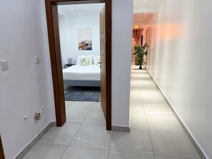 Ein Hotelgang mit einem Bett im Hintergrund, einem Blumentopf und einer Tür zu einem anderen Zimmer.