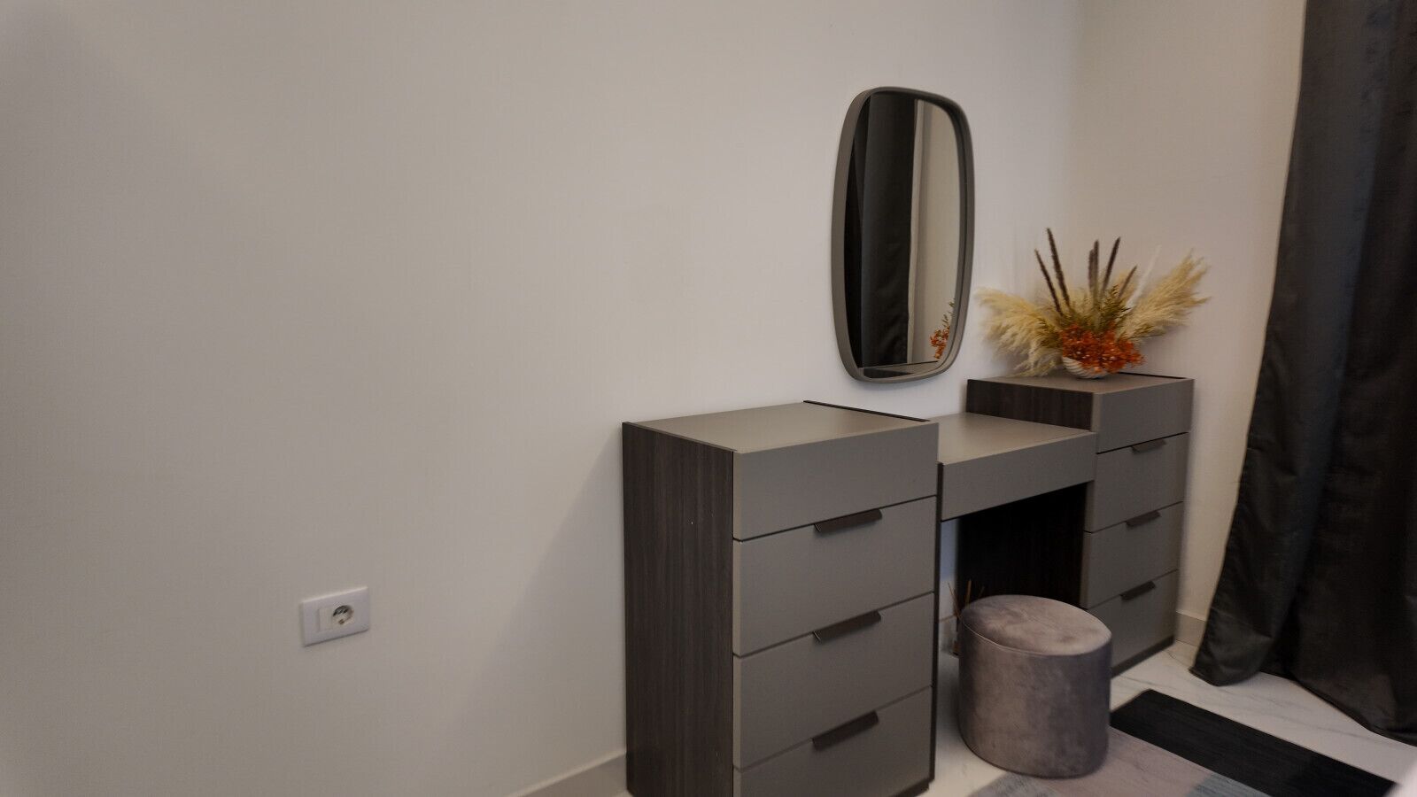 A modern bathroom vanity with a mirror, a small plant, and a cylindrical container.