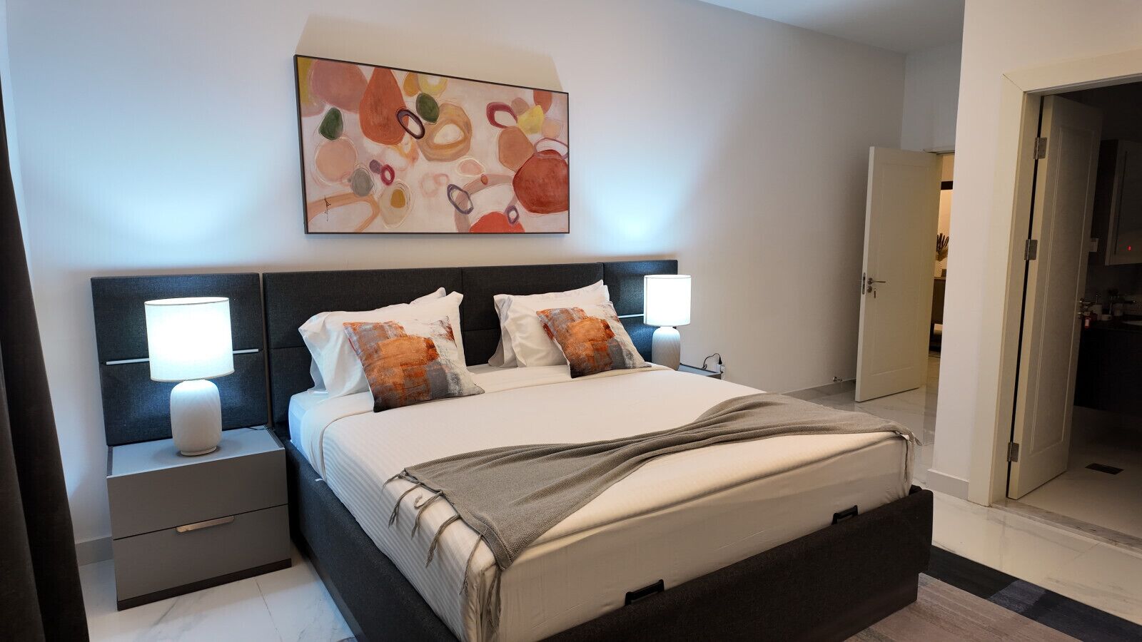 Een moderne slaapkamer met een bed, twee nachtkastjes, een wanddecoratie en een deur naar een inloopkast.