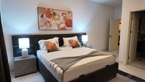 Un dormitorio moderno con una cama, dos mesitas de noche, una mesita auxiliar, una obra de arte en la pared y una puerta a un armario.