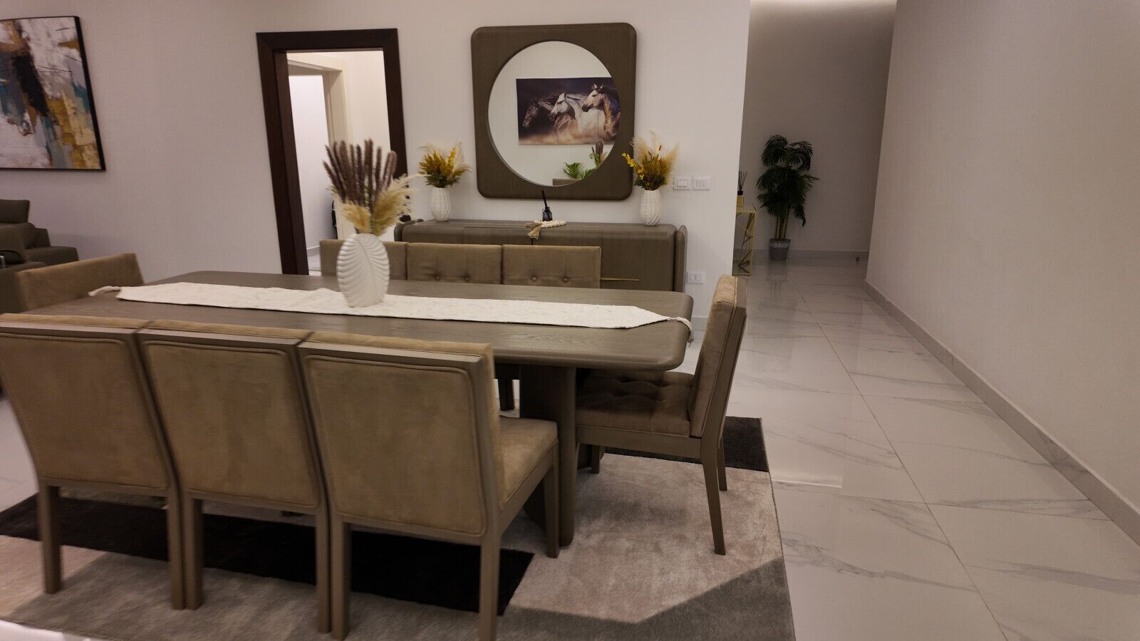 A dining area with a rectangular table, four chairs, a vase with dried plants, and a sofa.