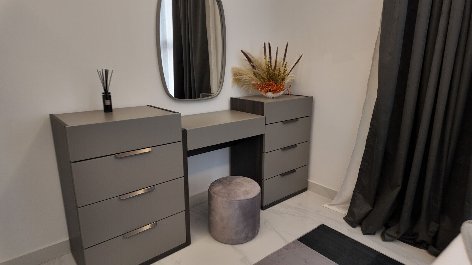 A modern bathroom with a grey vanity, a round stool, a mirror, and a decorative plant.