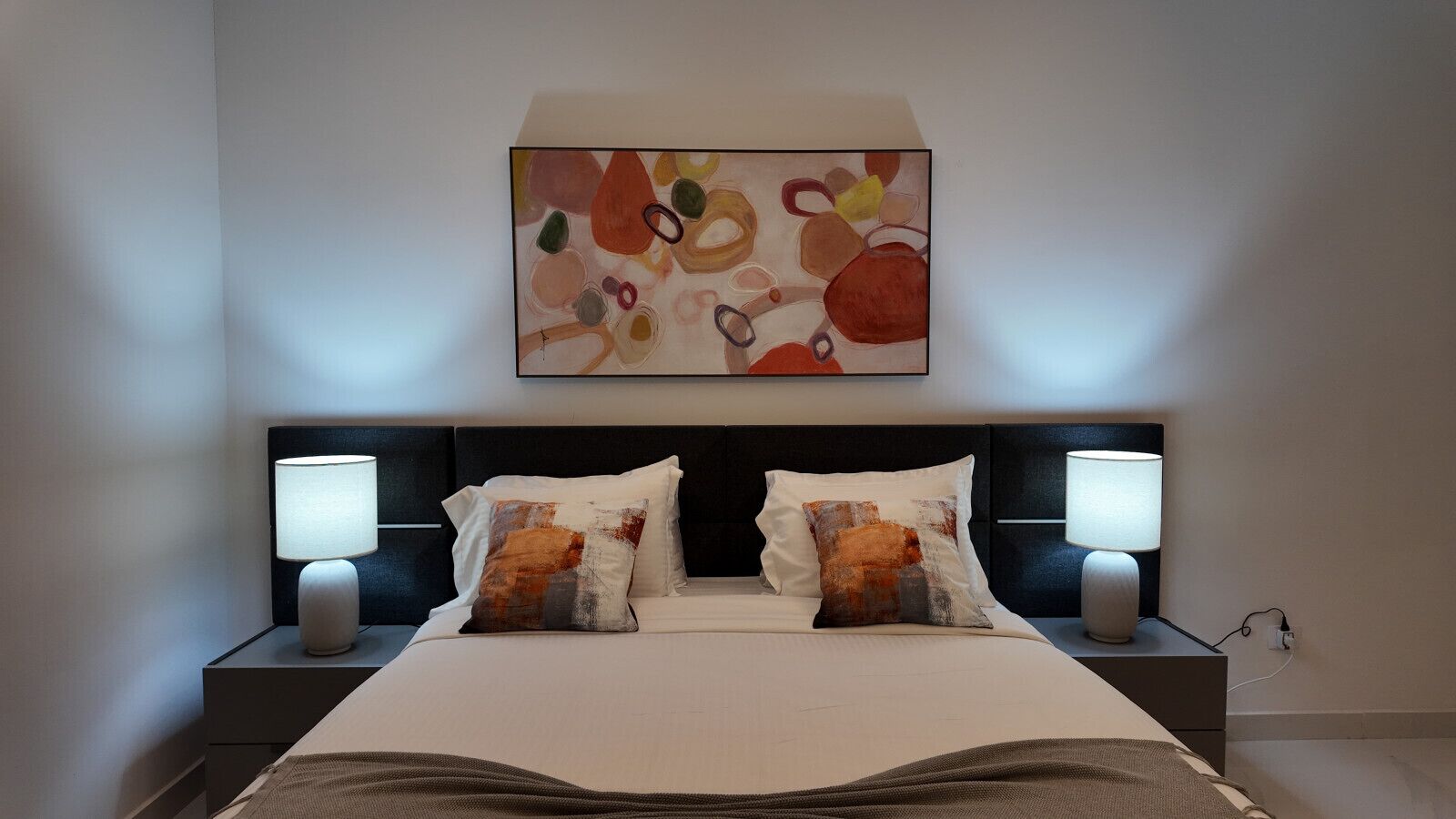 Ein Hotelzimmer mit einem Bett, zwei Nachttischlampen und einem Kunstwerk über dem Bett.