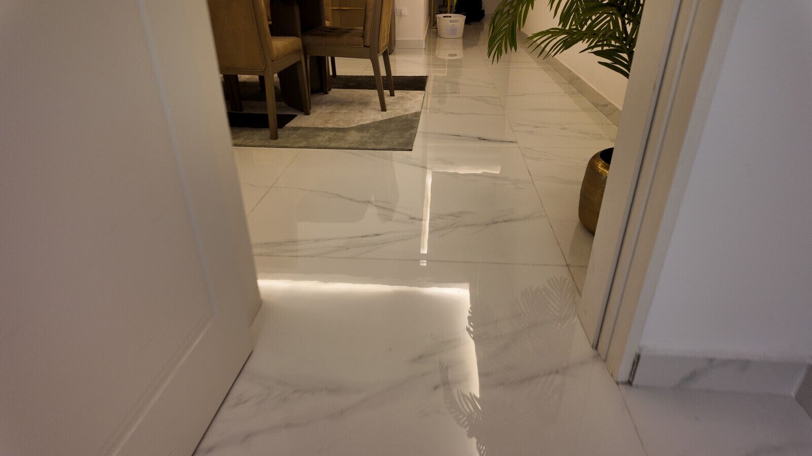 A hallway with a shiny marble floor, a dining area with chairs, and a potted plant.