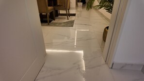 A hallway with a shiny marble floor, a dining area with chairs, and a potted plant.