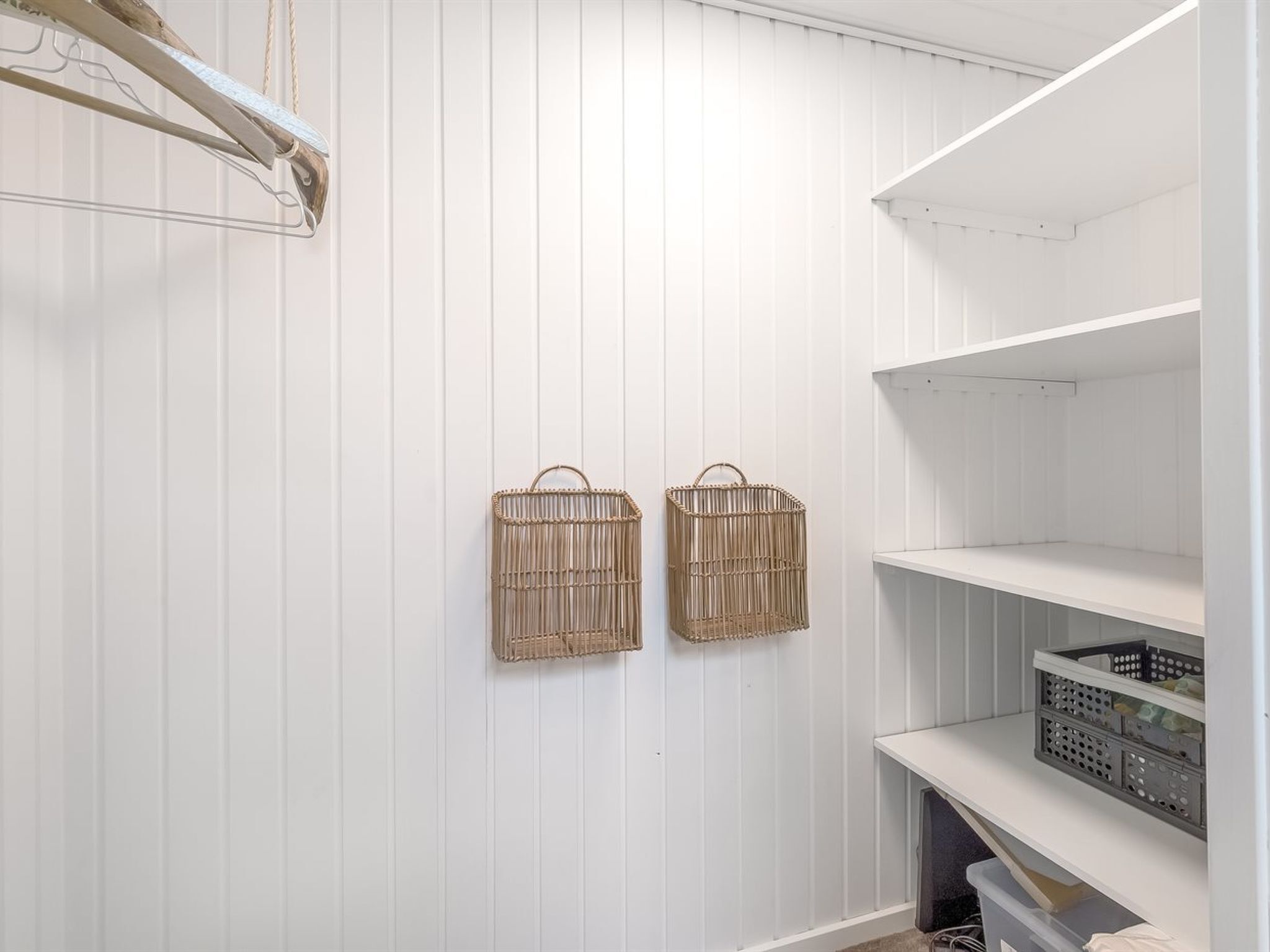 Un placard aux panneaux blancs, avec deux paniers en osier accrochés au mur et une étagère en dessous.