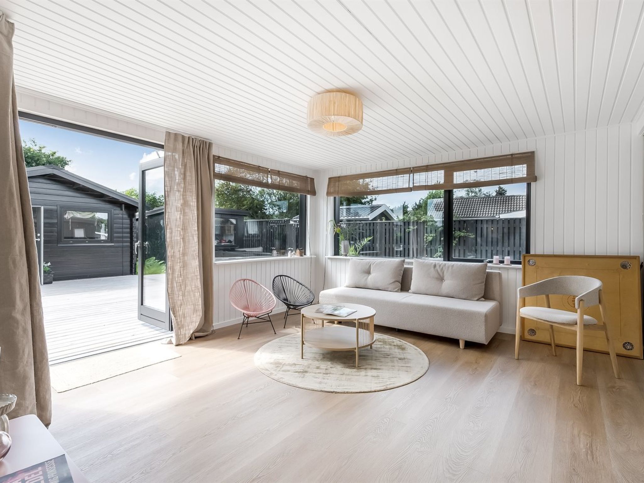 A modern living room with a sofa, coffee table, and chairs, large windows, and a sliding glass door leading to an outdoor area.