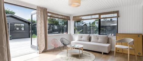 A modern living room with a sofa, coffee table, and chairs, large windows, and a sliding glass door leading to an outdoor area.
