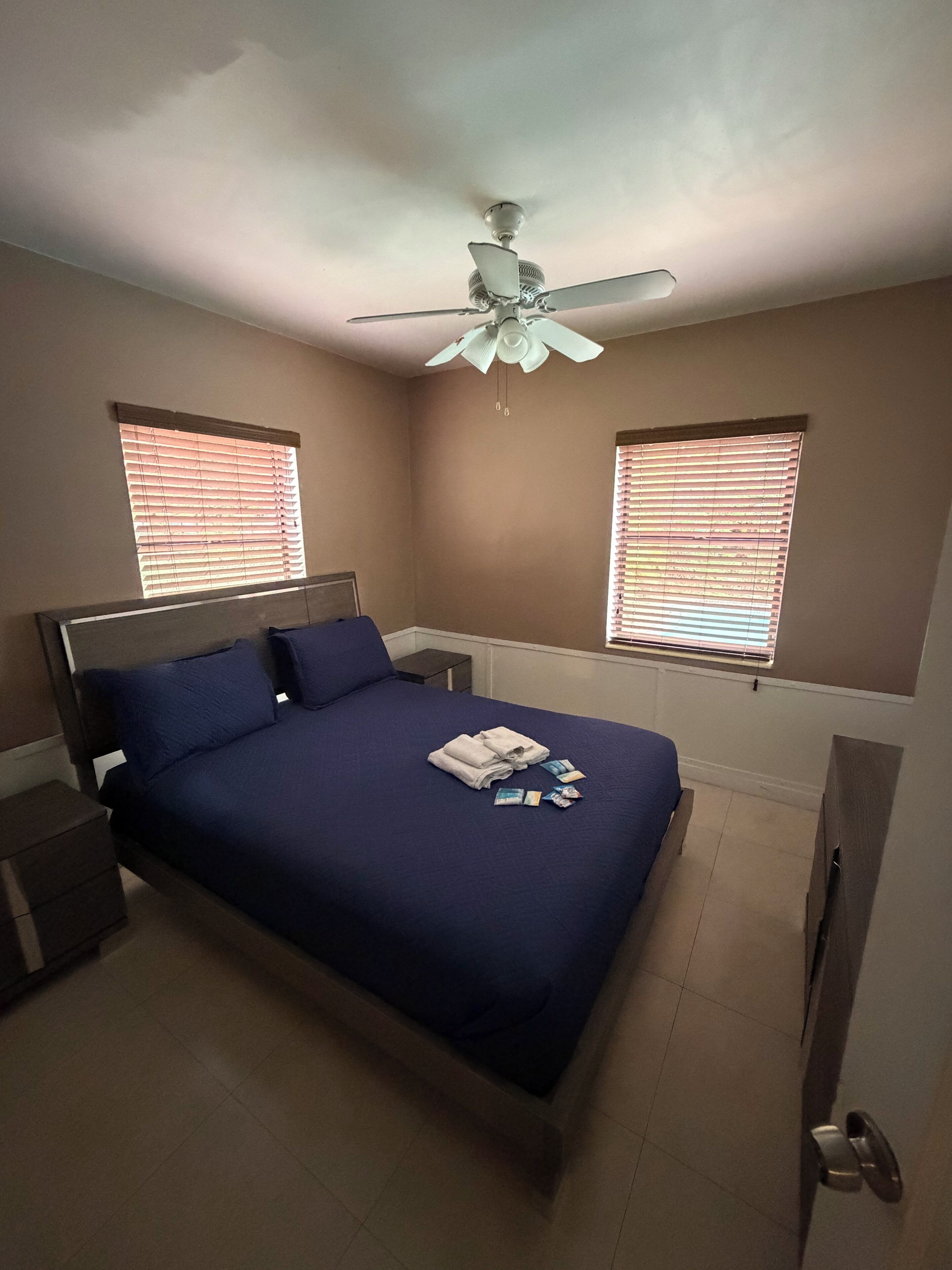 A bedroom with a bed, nightstands, a ceiling fan, and windows with blinds.