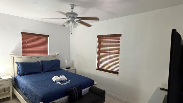A bedroom with a bed, bedside tables, a ceiling fan, and two windows with blinds. - Cozy 2-bedroom villa with Pool in sunny Miami (Miami)