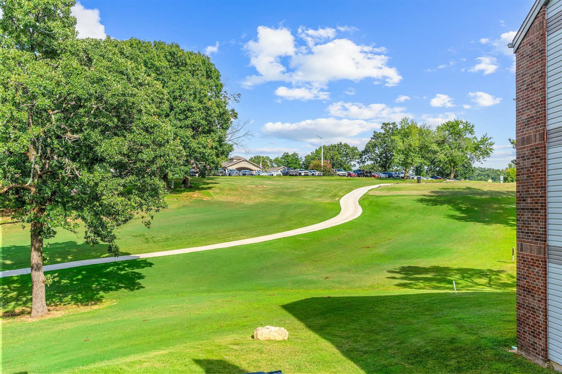 A golf course with a clear path, trees, and a building in the background.