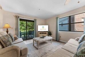 A living room with a sofa, a coffee table, a TV, and a sliding glass door leading to an outdoor area. - Birdie's Nest and 2BDR Condo (Branson)