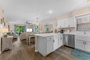 A modern kitchen with white cabinetry, a stainless steel dishwasher, and a dining area with a sofa and chairs. - Birdie's Nest and 2BDR Condo (Branson)