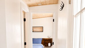 A narrow hallway leading to a bedroom with a bed, a nightstand, and a wall-mounted shelf.