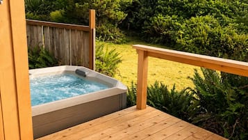 En træterrasse med et spabad og udsigt til en have med forskellige planter og et træ.