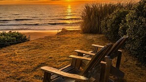 A sunset view over the ocean with a wooden chair and grass in the foreground.