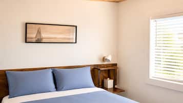 A bedroom with a bed, a nightstand, a framed picture, and a window with blinds.