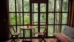 A room with a large window, wooden furniture, and a view of a forest. - Eco Quechua  (Santa Teresa)