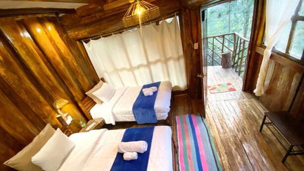 A wooden cabin with two beds, a bench, and a view of the outdoors. - Eco Quechua  (Santa Teresa)
