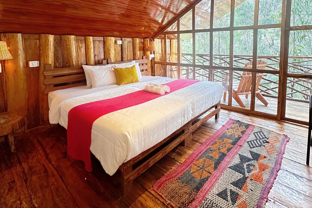 A wooden room with a bed, a window, and a view of greenery.