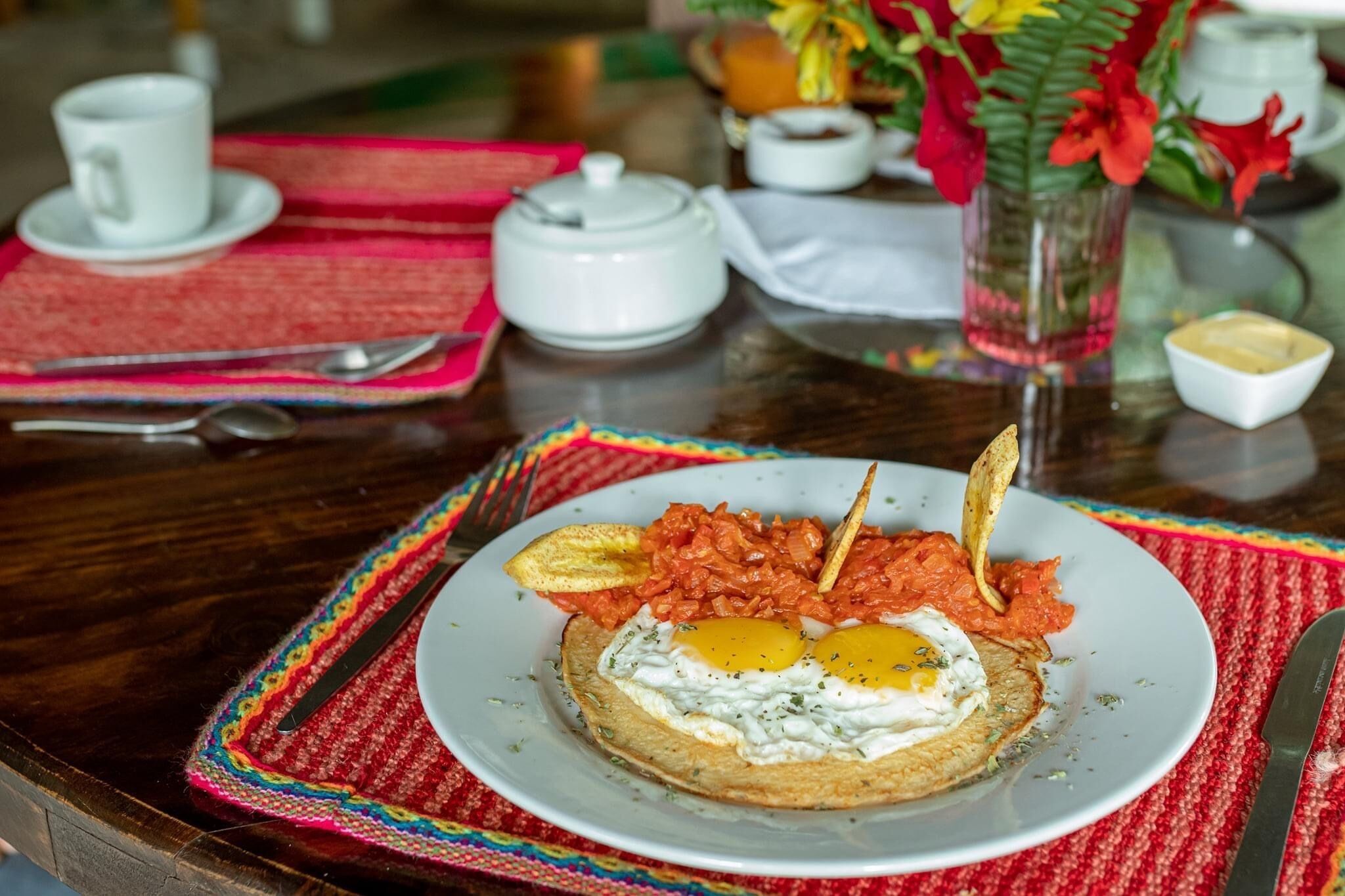 A breakfast plate with eggs, tomatoes, and toast on a table with a red placemat.