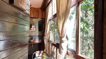 A wooden cabin interior with a dining area, a window with curtains, and a view of the outdoors.
