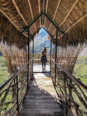 Un puente de madera con techo de paja que lleva a un paisaje montañoso.